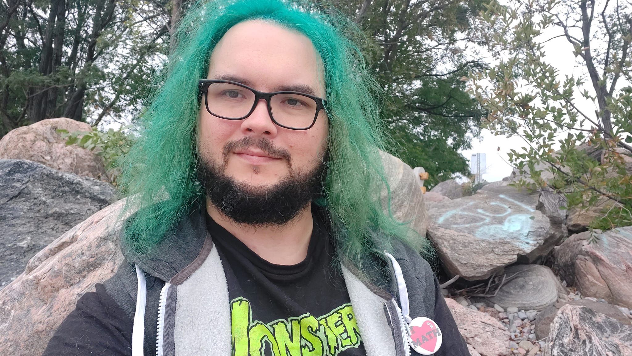 A man with green hair stands outside at a boulder breakwater, photo 3